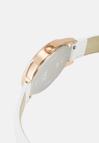 Roosa kuldne kell sileda ümaraga korpusega, valgest nahast rihmaga ja tekstureeritud krooniga. Tagaküljel on poleeritud pinnaga, millel on tootja andmed.