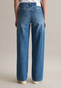 Blaue Denimweitbeinjeans mit hoher Taille, zwei Gesäßtaschen und Steppdetails. Der Stoff hat eine strukturierte, weiche Oberfläche.