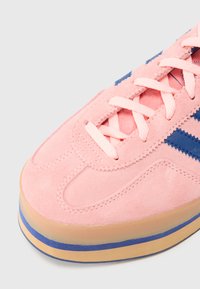 Roza semiš športni copat z modrimi poudarki, ki ima večplastno podplat in roza vezalke, prikazuje klasičen dizajn in teksturiran zaključek.