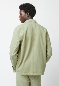 Lichtgroene denimjacket met een puntige kraag, zichtbare naden en lange mouwen. Heeft een rechte snit en een rugpasontwerp.