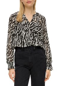 Blusa a strisce zebrate in bianco e nero, tessuto trasparente, design plissettato, scollatura a V, maniche lunghe con polsini elastici, abbinata a jeans neri a vita alta.