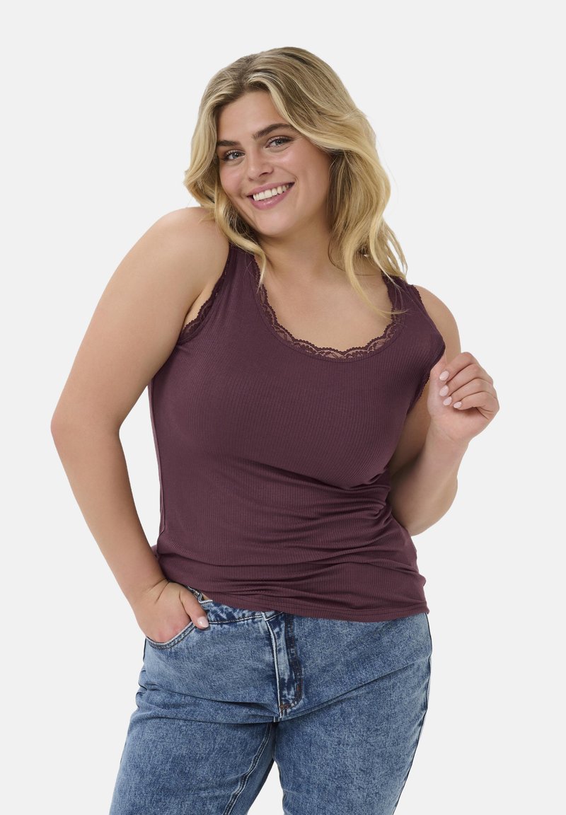 Fialový žebrovaný top s krajkovým lemem na výstřihu, spárovaný s lehkými modrými džíny. Modelka se usmívá, s jednou rukou v kapse.