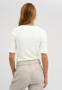 White ribbed short-sleeve top with a rounded neckline, paired with light gray textured high-waisted trousers featuring back pockets.
