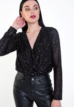 Black sequined blouse with long sleeves, deep V-neck, and textured surface. Worn with high-waisted black leather pants.