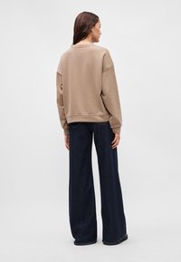 Μπεζ φανελάκι με χαλαρή εφαρμογή και ριγέ στρίφωμα, συνδυασμένο με τζιν ψηλής μέσης, φαρδιάς γραμμής σε σκούρο μπλε χρώμα. Λείο υλικό και χαλαρός σχεδιασμός.