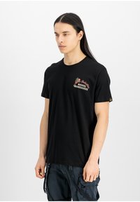 Černé bavlněné tričko s potiskem na levém prsu, obsahující text "Alpha Industries Naval Maneuvers" a květinové akcenty.
