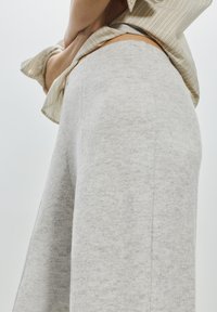 Pantalon de survêtement large gris clair en matière douce et texturée. Doté d'une taille haute et d'une coupe décontractée, posé sur un fond clair.