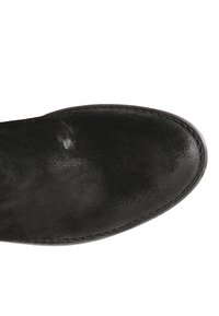 Musta mokka nilkkuri, jossa on pyöreä kärki, sileä pinta ja koristeellisia tikkejä pohjan ympäri. Ylhäältä katsottuna näkyy kevyt kiilto.