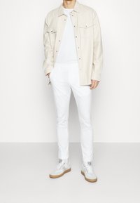 Witte katoenen broek gecombineerd met een lichtbeige overhemd met knopen en grijze sneakers met een beige zool. Zachte textuur, casual pasvorm.