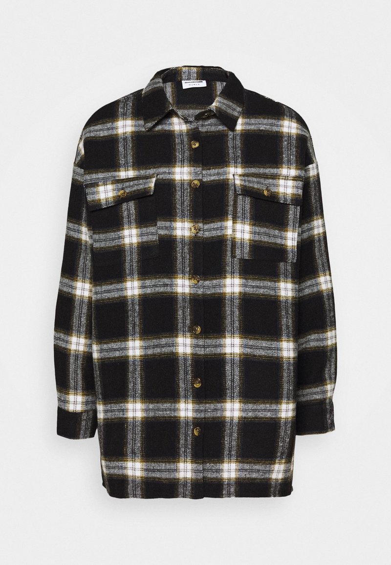 Chemise en flanelle à carreaux noir et blanc avec accents jaunes, fermeture boutonnée à l'avant, deux poches poitrine et manches longues. Texture douce, coupe décontractée.