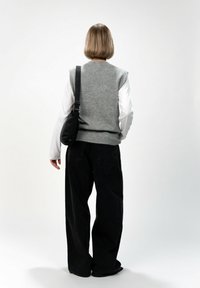 Gilet grigio lavorato a maglia sopra una camicia bianca a maniche lunghe, abbinato a jeans neri larghi. Una piccola borsa nera è indossata a tracolla.