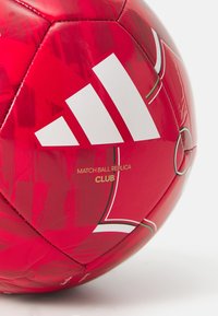 Rød fotball med en blank tekstur, med hvit Adidas-logo, gullskrift "MATCH BALL REPLICA CLUB," og grafiske mønstre på overflaten.