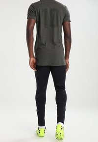 Šedé sportovní tričko s krátkým rukávem a číslem "10" na zádech, v kombinaci s černými legínami a jasně žlutými fotbalovými kopačkami.