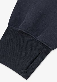 Puño de sudadera azul marino oscuro con textura acanalada, forro interior suave y un pequeño corte para mayor funcionalidad.