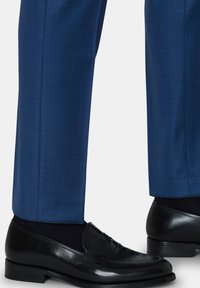 Blauwe op maat gemaakte broeken van een soepele stof, gecombineerd met zwarte loafers met een strakke uitstraling en subtiele textuur.