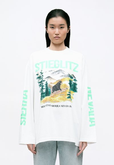 White long-sleeve t-shirt featuring a colorful bear graphic with mountains and trees, and bold, mint green text on the sleeves.