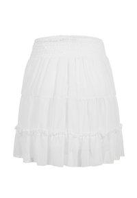Mini-jupe blanche à volants avec taille smockée et détail de volants à l’ourlet, tissu léger et fluide.