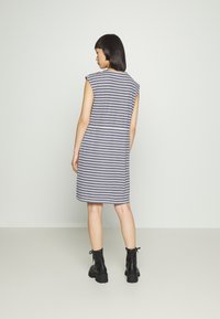 Vestido listrado, sem mangas, em cinza e branco, até ao joelho, com um corte descontraído. Usado com botas de tornozelo pretas com atacadores.