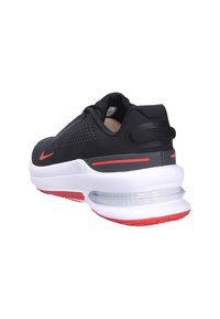 Zapatilla deportiva negra con parte superior de malla, acentos rojos y amortiguación de aire visible. Presenta una puntera redondeada y un cuello acolchado. La suela es blanca con rojo.