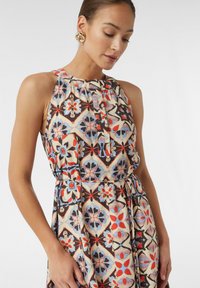 Ärmelloses bedrucktes Kleid mit Halterhals, farbenfrohen geometrischen Mustern in Rot, Schwarz, Blau und Creme, mit gerafftem Taillenbund und Seitentasche.