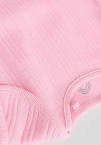 Ljusrosa bodysuit i mjukt tyg med horisontell ribbad struktur. Har rundad halsringning och slingrad detalj nära fållen.