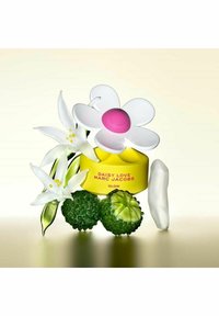 Daisy Love Marc Jacobs parfymflaska formad som en blomma, gul bas, rosa mitt, omgiven av vita liljor och gröna texturerade frukter.
