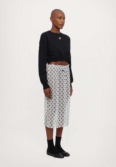 Black cropped sweatshirt with round neckline, paired with a white sheer skirt featuring a black crescent moon pattern, finishing below the knee.