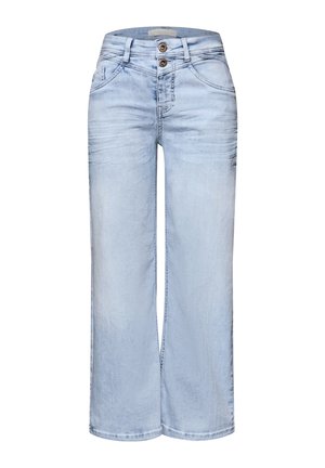 Person i lyseblå jeans og cropped navy- og hvidstribet sweater, iført sølvbangles på håndleddet, vist bagfra.