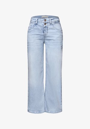 Osoba ubrana w jasnoniebieskie dżinsy i krótki granatowo-biały sweter w paski, nosząca srebrne bransoletki na nadgarstku, widziana od tyłu.