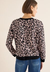 Różowy sweter w panterkę z czarnymi plamami, z czarnym prążkowanym dekoltem i mankietami, w połączeniu z niebieskimi dżinsami. Gładka faktura.