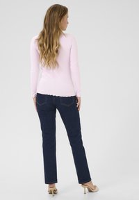 Haut à manches longues côtelé rose clair avec un ourlet festonné, associé à un jean droit bleu foncé. Le modèle est de dos.
