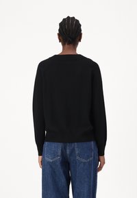 Pull en tricot noir avec une coupe décontractée, ourlet à côtes et manches longues. Il présente un col rond et un design de manches raglan.