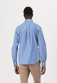 Blauw en witte gestreepte blouse met lange mouwen, een puntige kraag en rugplooi-details; gecombineerd met lichtbruine broeken.