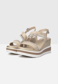 Sandales compensées beige avec plusieurs brides croisées, ornées de strass, présentant une plateforme texturée et une semelle en caoutchouc blanche.