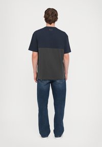 Kortermet T-skjorte med øvre del i marineblå og nedre del i mørkegrå, laget av myk bomull, parret med blå jeans.