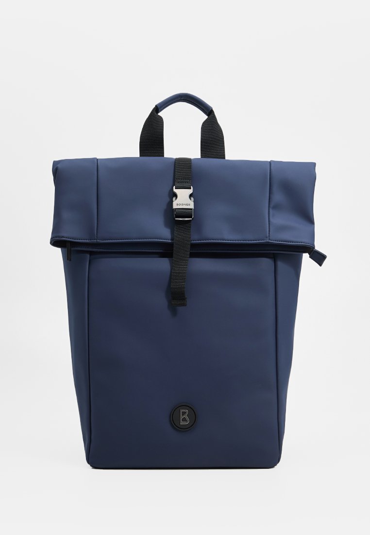 Granatowy plecak typu roll-top z czarnym regulowanym paskiem i metalowym zapięciem, górną rączką oraz okrągłym logo na przedniej kieszeni.