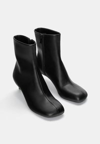 Bottines en cuir noir avec une texture lisse, fermeture éclair à l'arrière, forme de bout arrondi et un talon bas et fin.