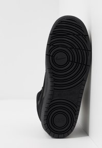 Sola de sapatilha preta com borracha texturizada, padrões de sulco circulares e a marca "Nike". Apresenta bordas lisas e um design sólido e escuro.