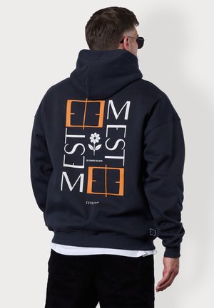 Dunkelblaues Kapuzensweatshirt mit einem grafischen Design in Weiß und Orange, einer Blume und quadratischen Akzenten. Weiches Material, verstellbare Kapuze.
