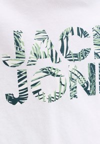 Λευκό ύφασμα με το κείμενο 'JAC JONI' γεμάτο με μοτίβα πράσινων και μαύρων τροπικών φύλλων.