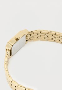 Montre-bracelet en ton or avec un boîtier rectangulaire, un bracelet à maillons et une finition polie. Elle est dotée d'une couronne proéminente et d'un fond gravé.