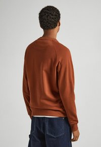 Felpa color ruggine con collo a giro, polsini e orlo a costine. Tessuto morbido e testurizzato con una vestibilità comoda e maniche raglan.