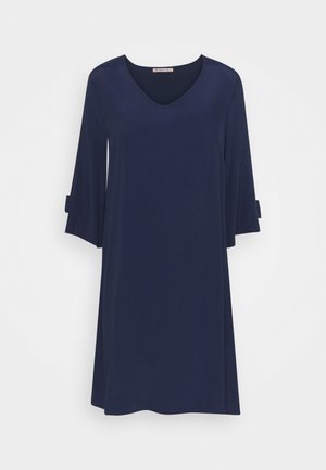 Robe bleu marine longueur genou avec manches cloche trois-quarts et décolleté en V suspendue sur un fond blanc.
