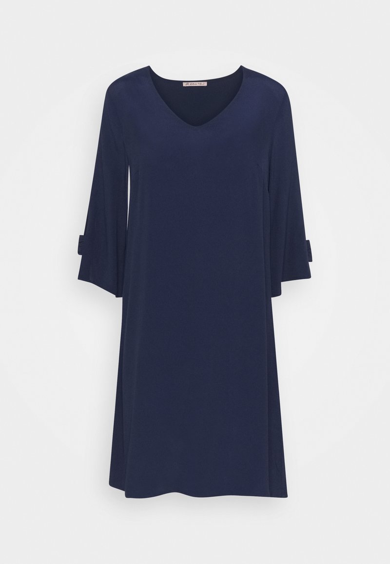 Robe bleu marine longueur genou avec manches cloche trois-quarts et décolleté en V suspendue sur un fond blanc.
