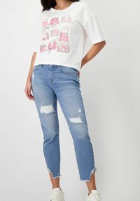 Bílý bavlněný tričko s barevnými ilustracemi kabelek, spárované s světle modrými džíny s roztrhanými detaily a třepenými okraji.