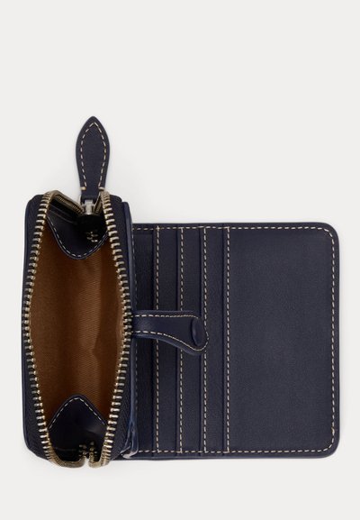 Portefeuille en cuir bleu marine avec coutures beiges, poche munie d'une fermeture éclair ouverte, quatre emplacements pour cartes, et fermeture à rabat avec bouton-pression sur fond blanc.