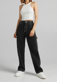 Svarta vida byxor med kontrasterande vit sömnad, hög midja och sidofickor. Kombineras med en figurnära vit halternecktop och vita sneakers.