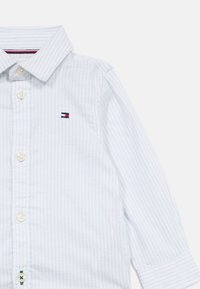 Svetlomodrá a bielo pruhovaná košeľa s dlhými rukávmi a zapínaním na gombíky, s malým logom na hrudi a jednoduchými manžetami.