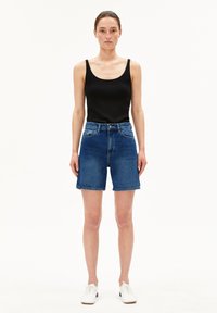 Shorts en denim de bleu moyen avec une coupe décontractée, taille haute et ourlet brut. Associés avec un débardeur noir à côtes et des chaussures blanches.