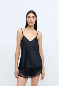 Camiseta de satén negro con tirantes finos y escote en V, combinada con pantalones cortos a juego que presentan bordes de encaje con forma de ondas. Textura suave y ajuste relajado.